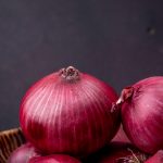 close-up view of red onions on maroon background with copy space