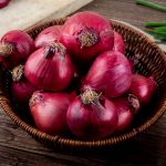 side view of basket full of red onions on wooden background